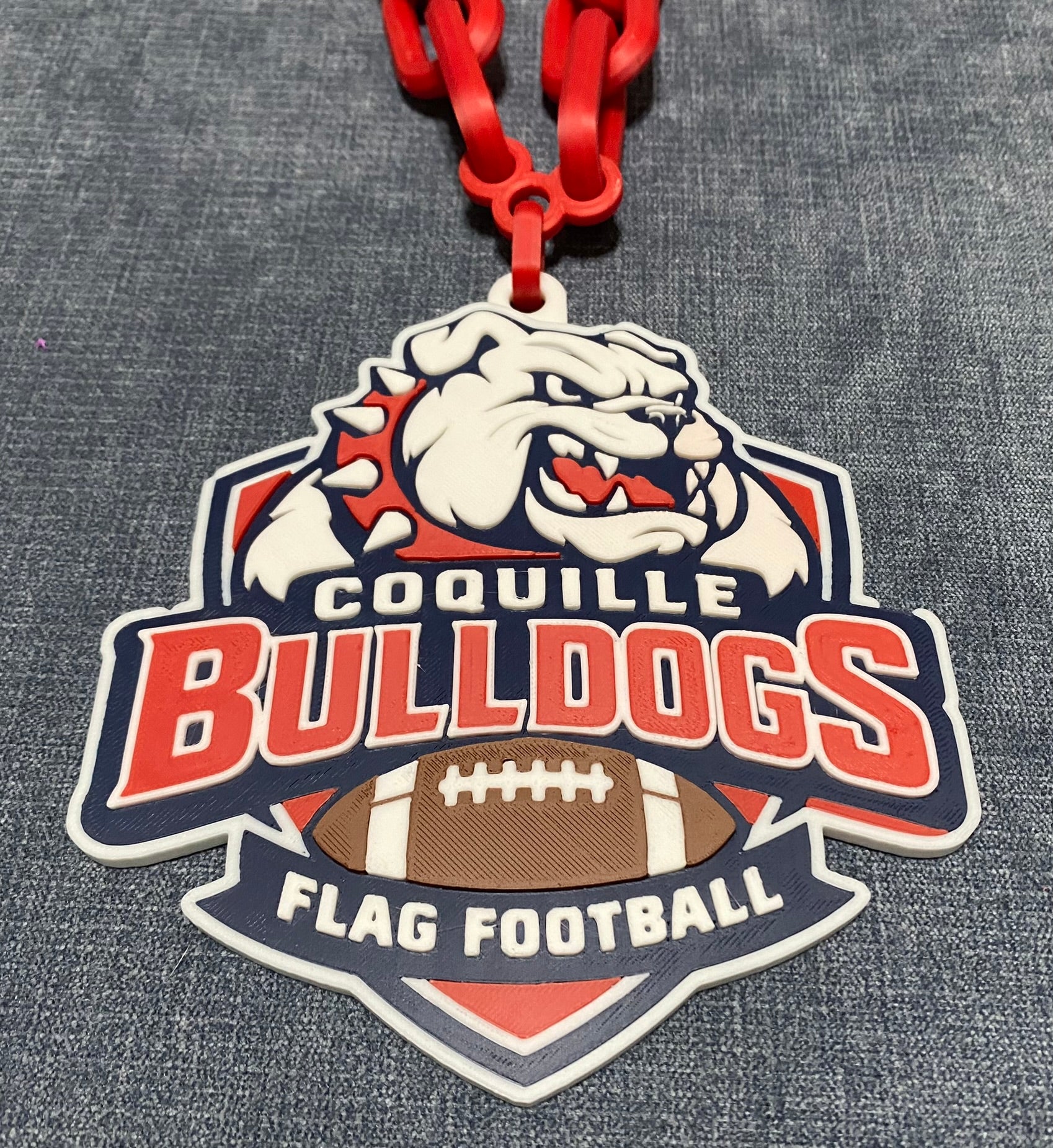 Coquille Bulldogs flag football logo on a red chain. Raised letters and design. 