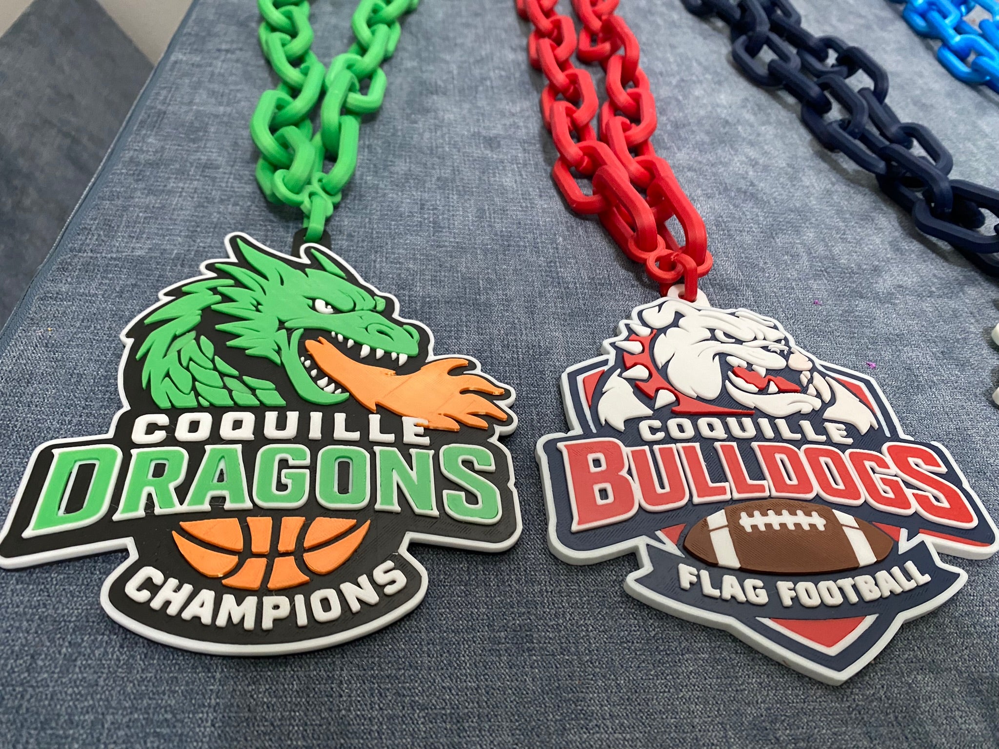 Two sports team Hustle Chains, one for Coquille Dragons and one for Coquille Bulldogs, on a textured surface. Basketball and Football.